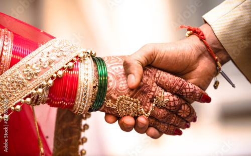 Indian Hindu Couple holding each other hands during their marriage symbolising love and affection. Hands of bride is decorated beautifully by indian mehndi art alongwith jewellery and colorful bangles