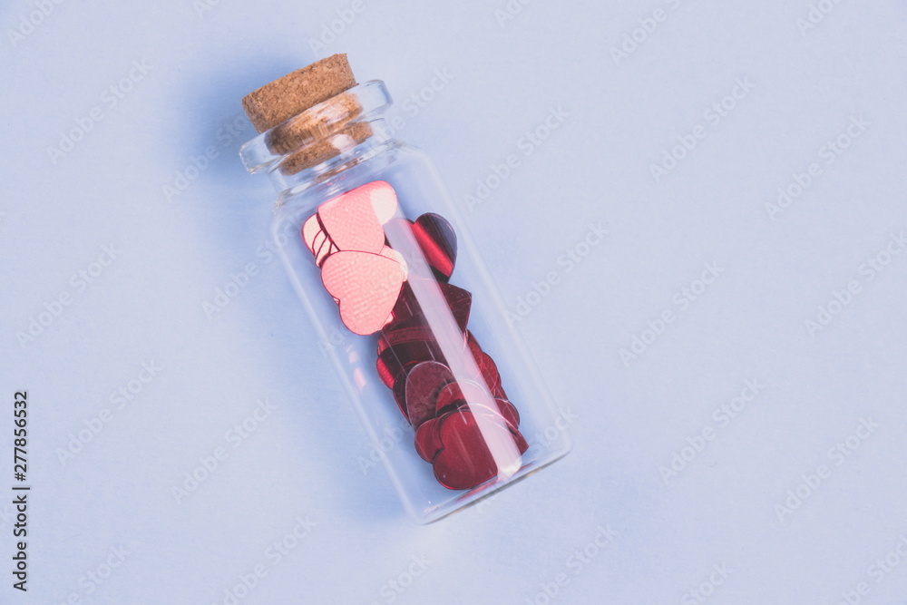 Naklejka premium Flat lay. Confetti in the form of heart in a decorative bottle on a light blue background.