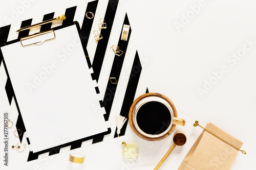 Flat lay desk table. Workspace with modern gold and black clipboard, stationery and a cup of coffee on white table. Mock-up, top view.