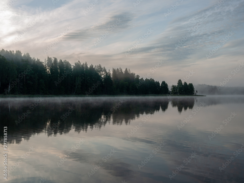 Foggy and mystical lake landscape before sunrise. All silhouettes are blurry and unclear. Vaidavas lake, Latvia