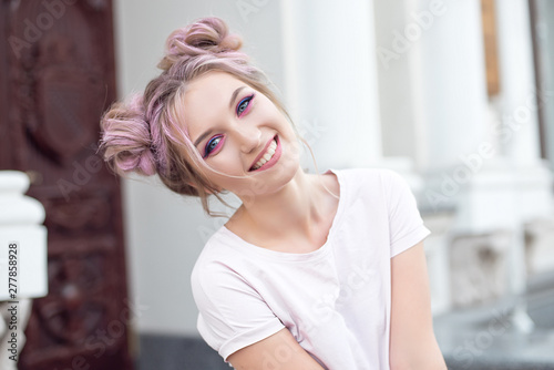 Happy cheerful young woman wearing her pink hair in a bun rejoicing at positive news or a birthday present, looking at the camera with a joyful and charming smile. Ginger student girl resting in the