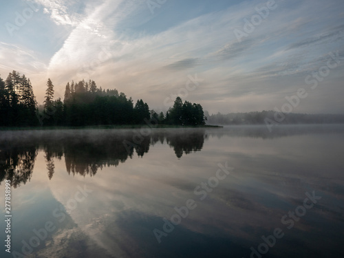 Foggy and mystical lake landscape before sunrise. All silhouettes are blurry and unclear. Vaidavas lake, Latvia