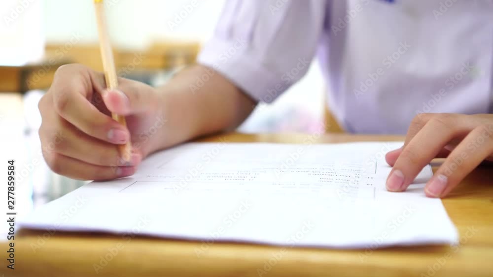 School or university students hands taking exams, writing examination room with holding pencil on optical form answers paper sheet on desk doing final test in classroom. Education assessment Concept School or university students hands taking exams, writing examination room with holding pencil on optical form answers paper sheet on desk doing final test in classroom. Education assessment Concept