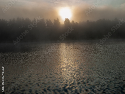 Foggy and mystical lake landscape before sunrise. All silhouettes are blurry and unclear. Vaidavas lake, Latvia