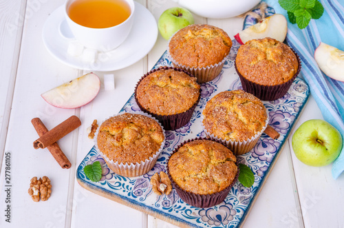 Homemade crispy apple muffins with walnuts and cinnamon on a white wooden background.