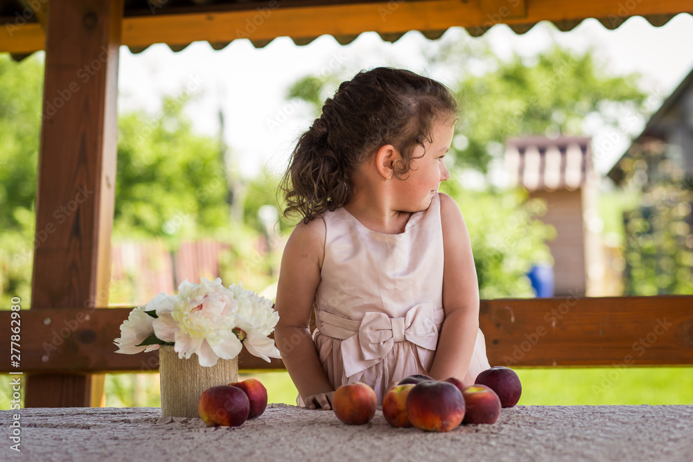 Fototapeta premium little girl at the table with peaches on nature in summer
