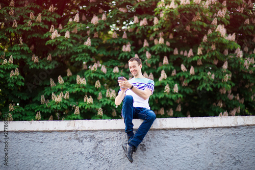 Smiling man with smartphone in hand sitting in street and using messenger. social networking concept