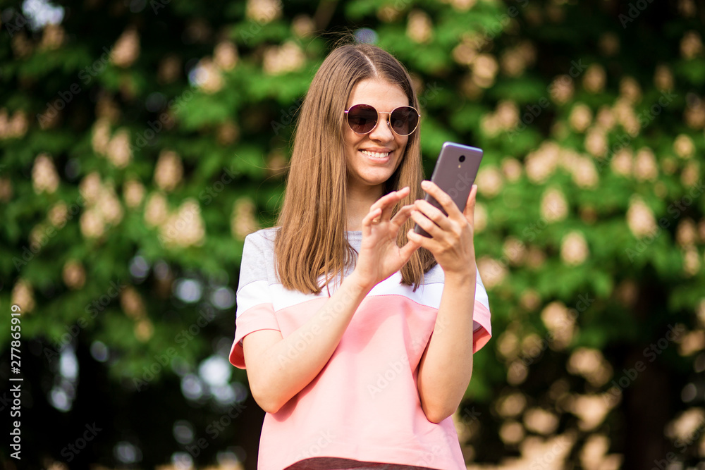 Woman wearing pink shirt texting on the smart phone walking in the street in a sunny day