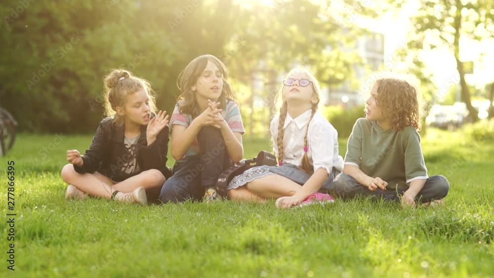 Cheerful and friendly classmates chatting while sitting on the grass in the park during a school break. Back to school, the students after lessons Cheerful and friendly classmates chatting while sitting on the grass in the park during a school break. Back to school, the students after lessons