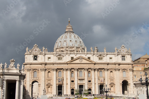 Main facade and dome of Saint Peter's Basilica seen from Saint Peter's Square with rainy clouds on background, Vatican city state, Italy.