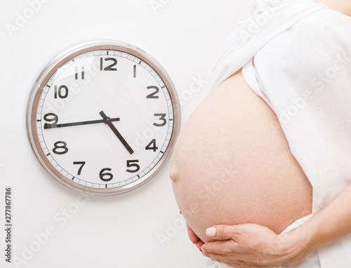 Pregnant woman with clock on a wall during final weeks of pregnancy
