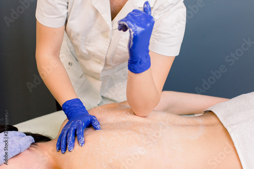 Professional back and body massaging to beautiful girl in cosmetology cabinet or beauty parlor. Hands of woman cosmetologist in blue gloves