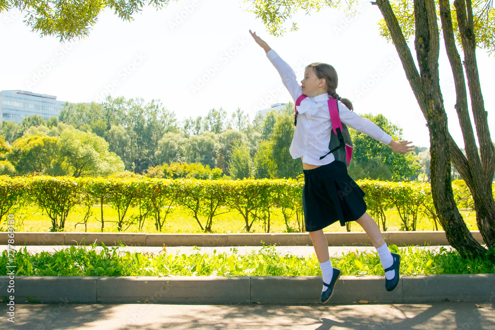 in the park, in the fresh air, a schoolgirl is having fun and jumping up, raising her hand