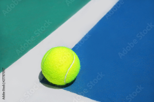 Summer sport concept with tennis ball on white line in the corner of hard tennis court. Flat lay, top view, copy space. Blue and green. © IrynaV
