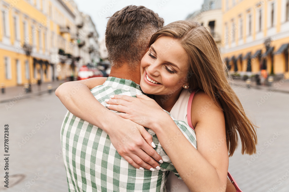 Image of happy young couple smiling and hugging together while walking through city street Image of happy young couple smiling and hugging together while walking through city street