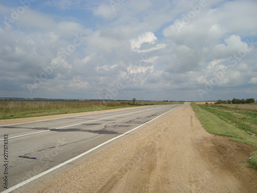 Direct asphalt road through the countryside under the sky, on which the clouds float.