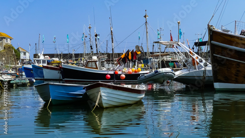 Colourful view of an English coastal harbour, with fishing boats at anchor. Moored skiffs and dinghies. Summer landscape image with reflections. Distant quayside with houses.