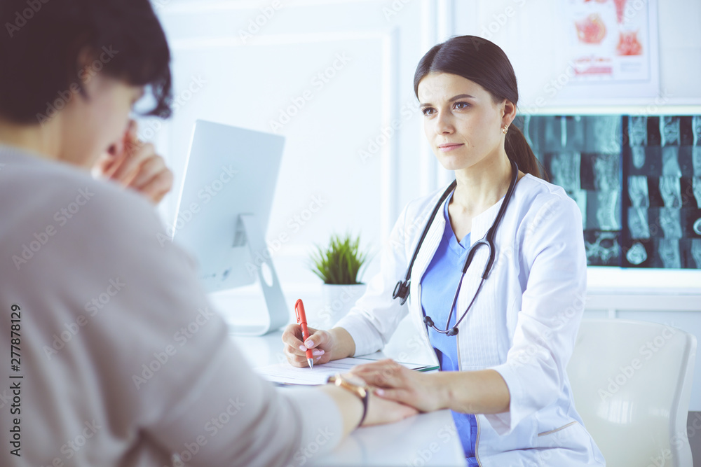 Female doctor calming down a patient at a hospital consulting room, holding her hand Female doctor calming down a patient at a hospital consulting room, holding her hand