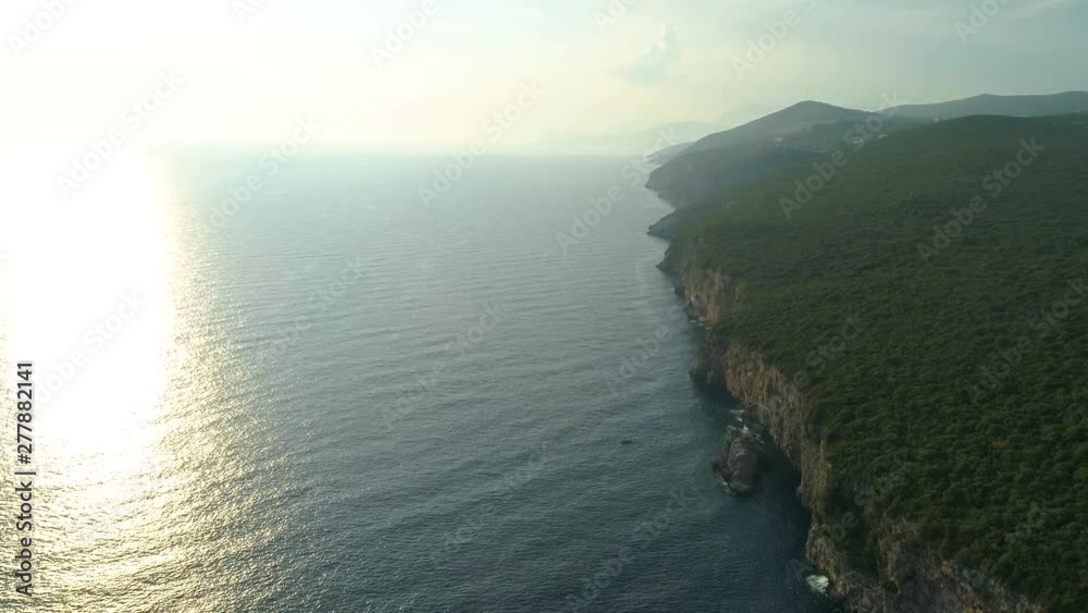 Aerial view above Montenegro lush green coastal cliff edge overlooking sparkling sunset seascape. Aerial view above Montenegro lush green coastal cliff edge overlooking sparkling sunset seascape.