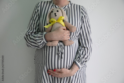 A pregnany woman holding her tummy and a bunny teddy bear photo