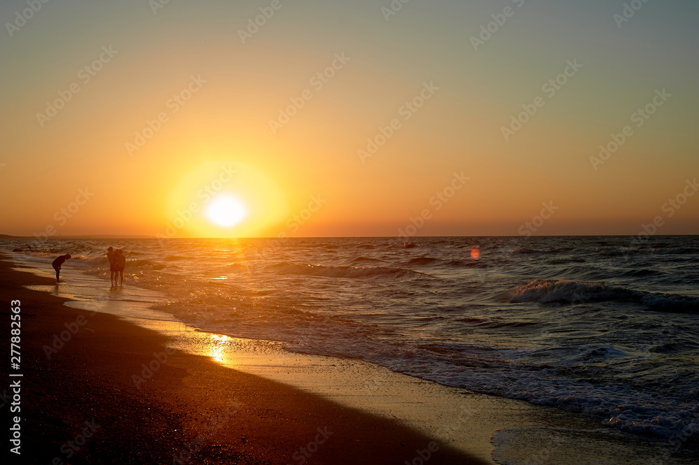 Sea Golden sunset. Waves run on the sandy shore. Silhouettes of people walking along the shore.