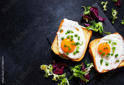 Sandwich with ham, cheese and egg. A traditional French croque-madame sandwich served with lettuce leaves on a black plate. Popular French cafe meal. Black background. Top view. Space for text photo