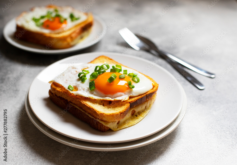 Sandwich with ham, cheese and egg. A traditional French croque-madame sandwich served on a white plate. Popular French cafe meal. Gray background. Close-up. Space for text