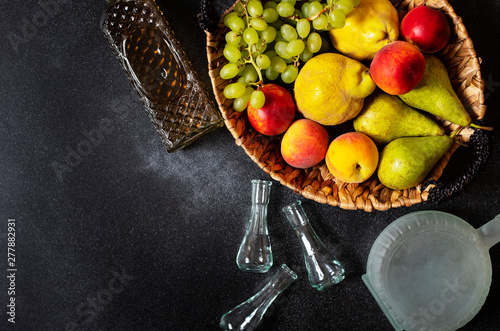 Rakia or Rakija the traditional balkan fruit brandy. The fruits of which produce Rakia. Fruits in a basket, bottles and glasses for alcohol. Top view. Black background. Space for text photo