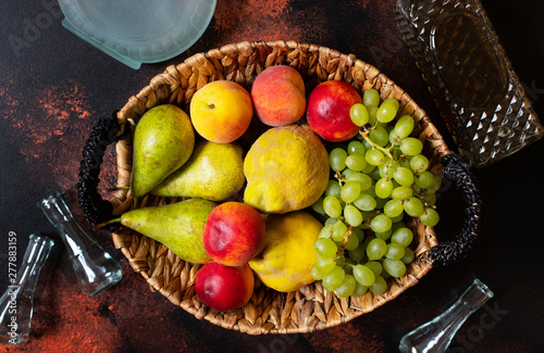 Rakia or Rakija the traditional balkan fruit brandy. The fruits of which produce Rakia. Fruits in a basket, bottles and glasses for alcohol. Top view. Dark vintage background. Space for text photo