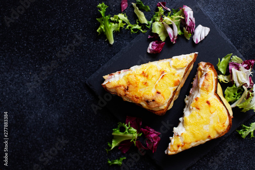 Sandwich with ham, cheese and bechamel sauce. A traditional french croque-monsieur sandwich served with lettuce leaves on a black plate. Black background. Top view. Space for text