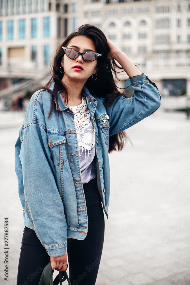 Interested glamorous woman in oversized denim jacket makes selfi. Gorgeous brunette girl posing on city background