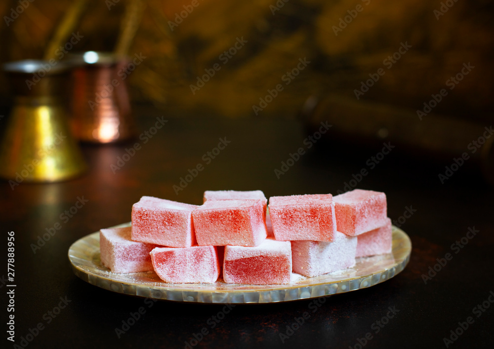 Rosewater-flavored Turkish Delight or Rahat Lokum (Loukoumi, Ratluk) on a vintage plate. In the background are two copper vintage cezves and a coffee grinder. Golden background. Front view. Copy space