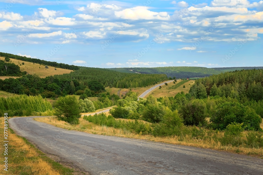 Travel and tourism. Landscape, road stretching into the distance among beautiful green forests and hills on a summer day in good weather against a blue sky