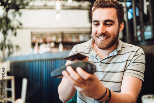 Smiling man making a wireless payment, customer using mobile phone, device with nfc technology for paying the bill