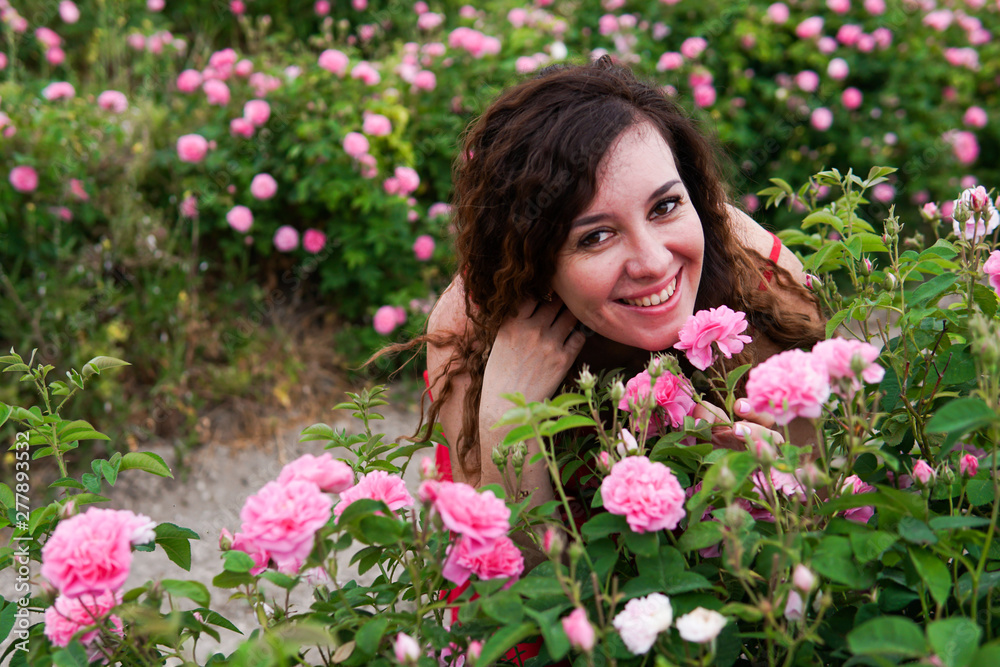 Beautiful woman in red dress on a field of blossoming roses Beautiful woman in red dress on a field of blossoming roses