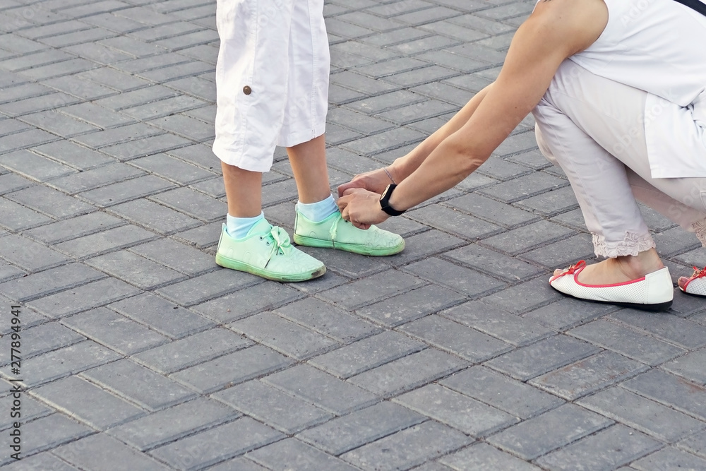 adult girl tying shoelaces on sneakers to her daughter