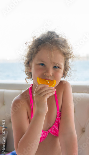 Baby with orange. Happy little girl eating orange near the sea.