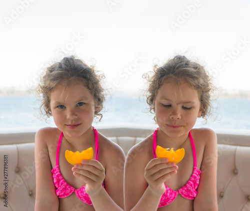 Children with oranges. Happy little girls eat oranges near the sea. Photo collage.