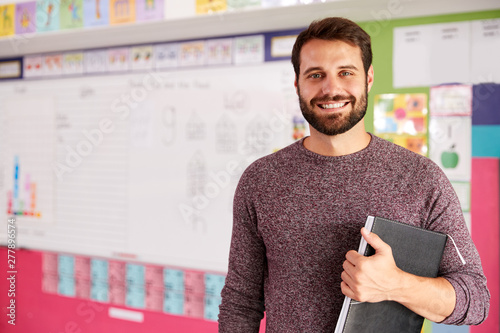 Portrait Of Male Elementary School Teacher Standing In Classroom photo