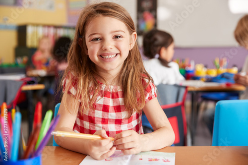 Portrait Of Smiling Female Elementary School Pupil Working At Desk