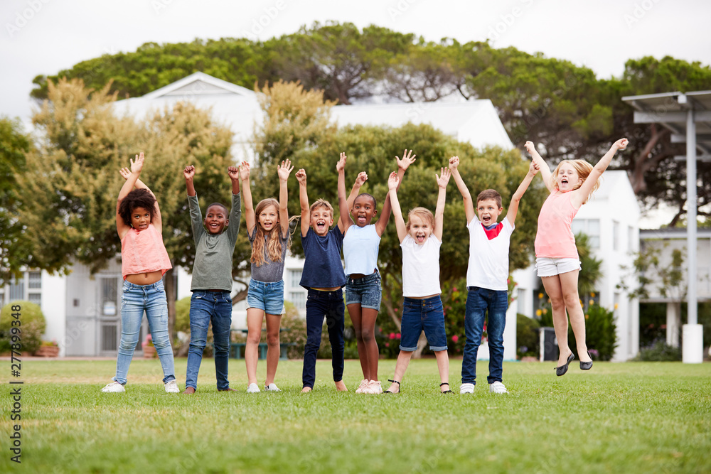 Obraz premium Group Of Excited Elementary School Pupils Standing On Playing Field At Break Time With Arms Raised