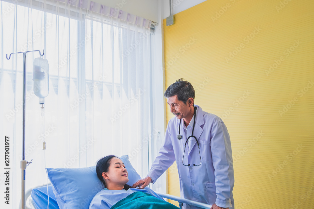Senior asian male doctor visiting middle-aged female patient on the bed in room hospital.
