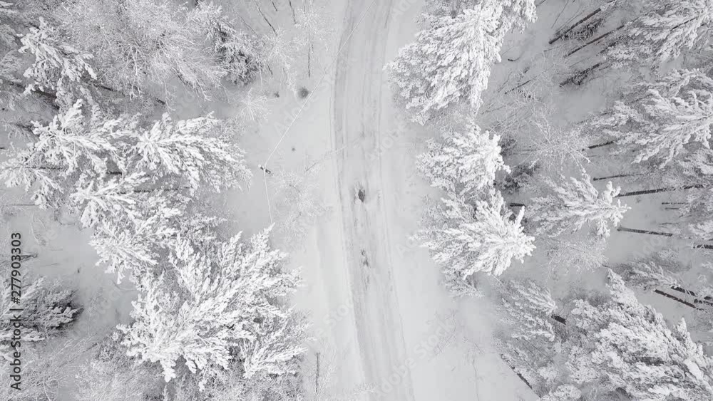 Vertical aerial view of passenger car driving slowly on a snowy forest road in Finland. Vertical aerial view of passenger car driving slowly on a snowy forest road in Finland.