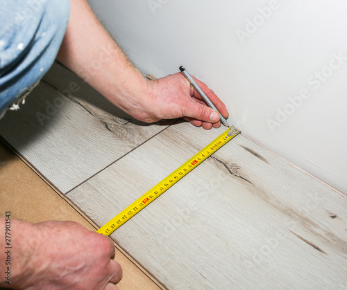 Worker making laminate flooring in apartment. Measure tape and pencil in hands. Maintenance repair renovation. Wooden parquet planks indoors.