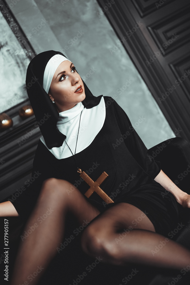 Sexy nun prays indoor . Beautiful young holy sister. Young beautiful nun  with a cross in a robe in a black interior. Stock Photo | Adobe Stock