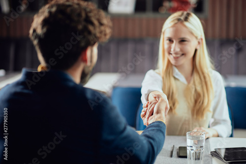 Two business partners shaking hands while sitting in coffee shop.