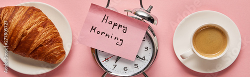 top view of alarm clock with happy morning lettering on sticky note near coffee and croissant on pink background, panoramic shot