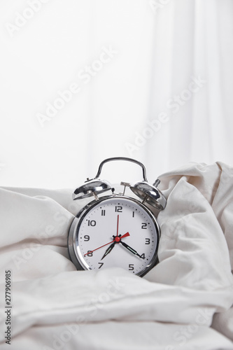 silver alarm clock in blanket in white bed