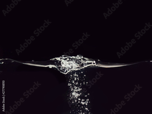 Droplet of water dropped into liquid isolated on black background, close up view. Rippling surface and bubbles underwater. Abstract background for overlays design, screen blending mode layer