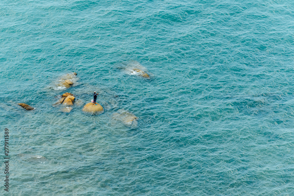 Aerial view of Fisherman standing on the stones amid the sea wave for fishing in Chonburi, Thailand.